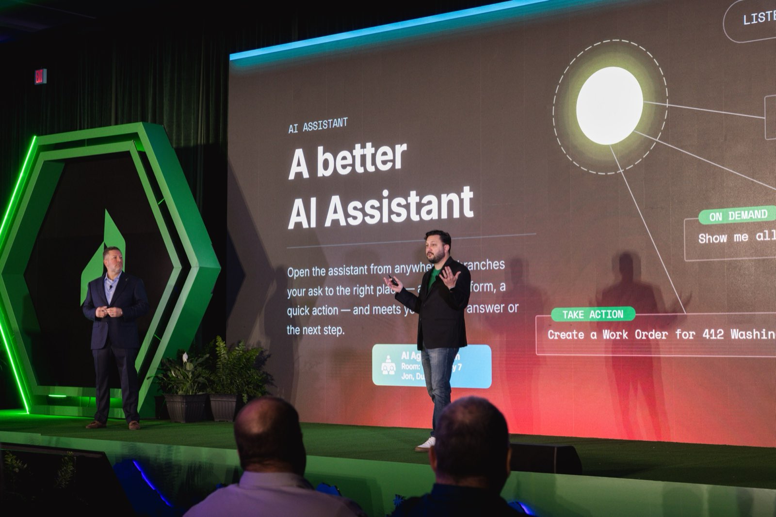 Jake on the Be Herd main stage in front of a slide reading A better AI Assistant